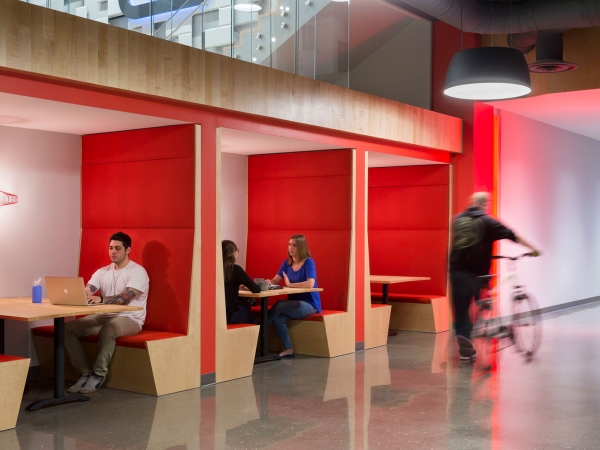People sitting in booths in an office space and a person strolling by on a bicycle.