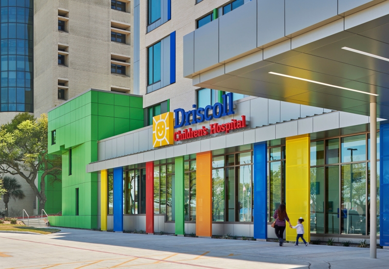 A parent and child walking in front of a colorful hospital building. 